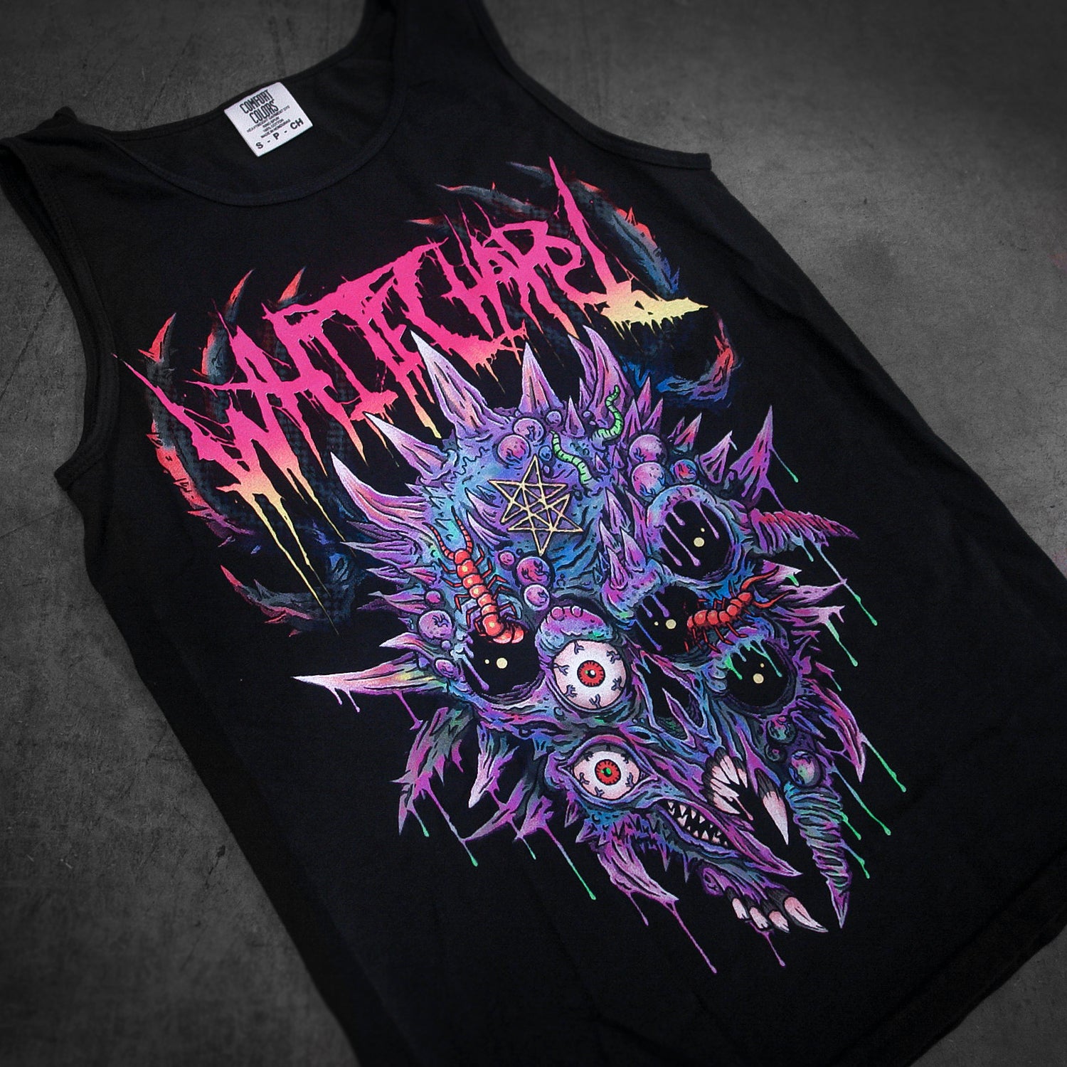 A black Comfort Colors tank top by Whitechapel featuring “WITCHARD” in jagged, colorful letters above a striking multi-eyed demonic skull graphic in purple, blue, and red—ideal for fans of bold printed garments.