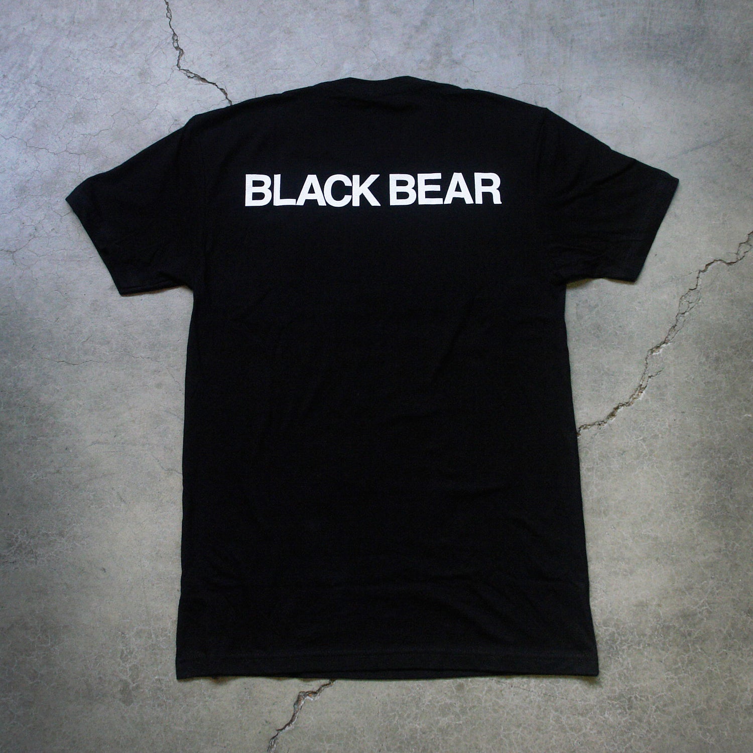  Image of the back of a black tshirt against a grey concrete background. The back of the shirt says black bear across the shoulders in white text.