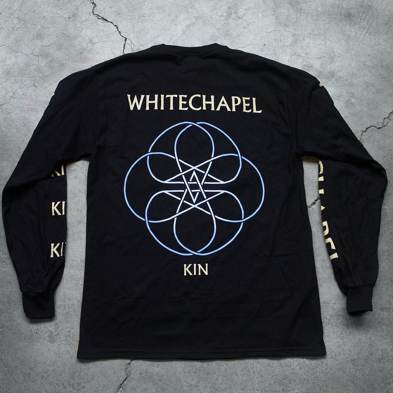 Image of the back of a black longsleeve against a grey concrete background. The left sleeve says 