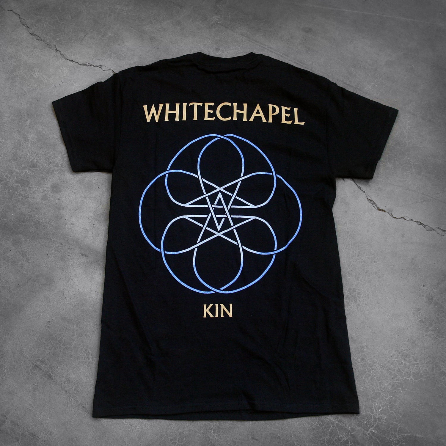 image of the back of a black tee shirt on a cracked concrete background. The back reads 