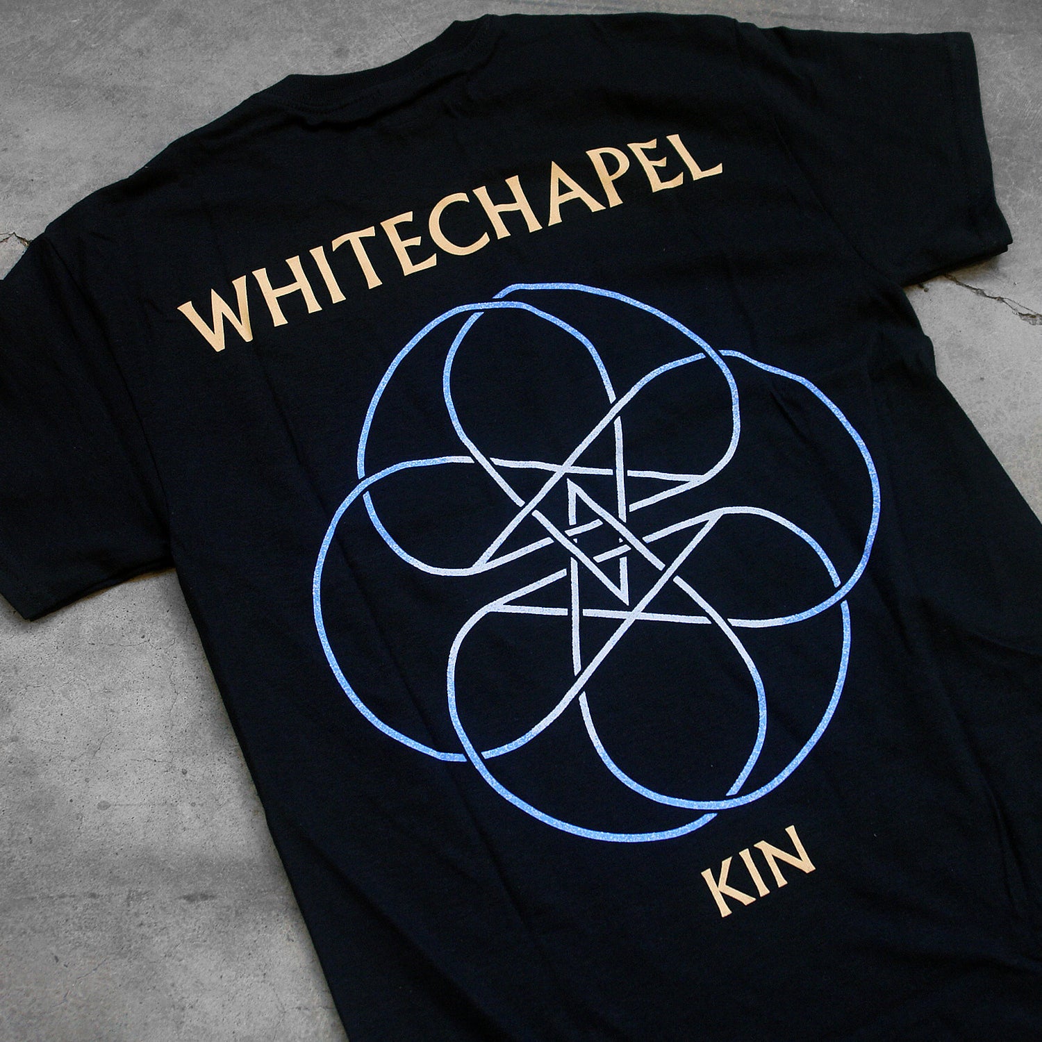 close up, angled image of the back of a black tee shirt on a concrete background. The back reads 