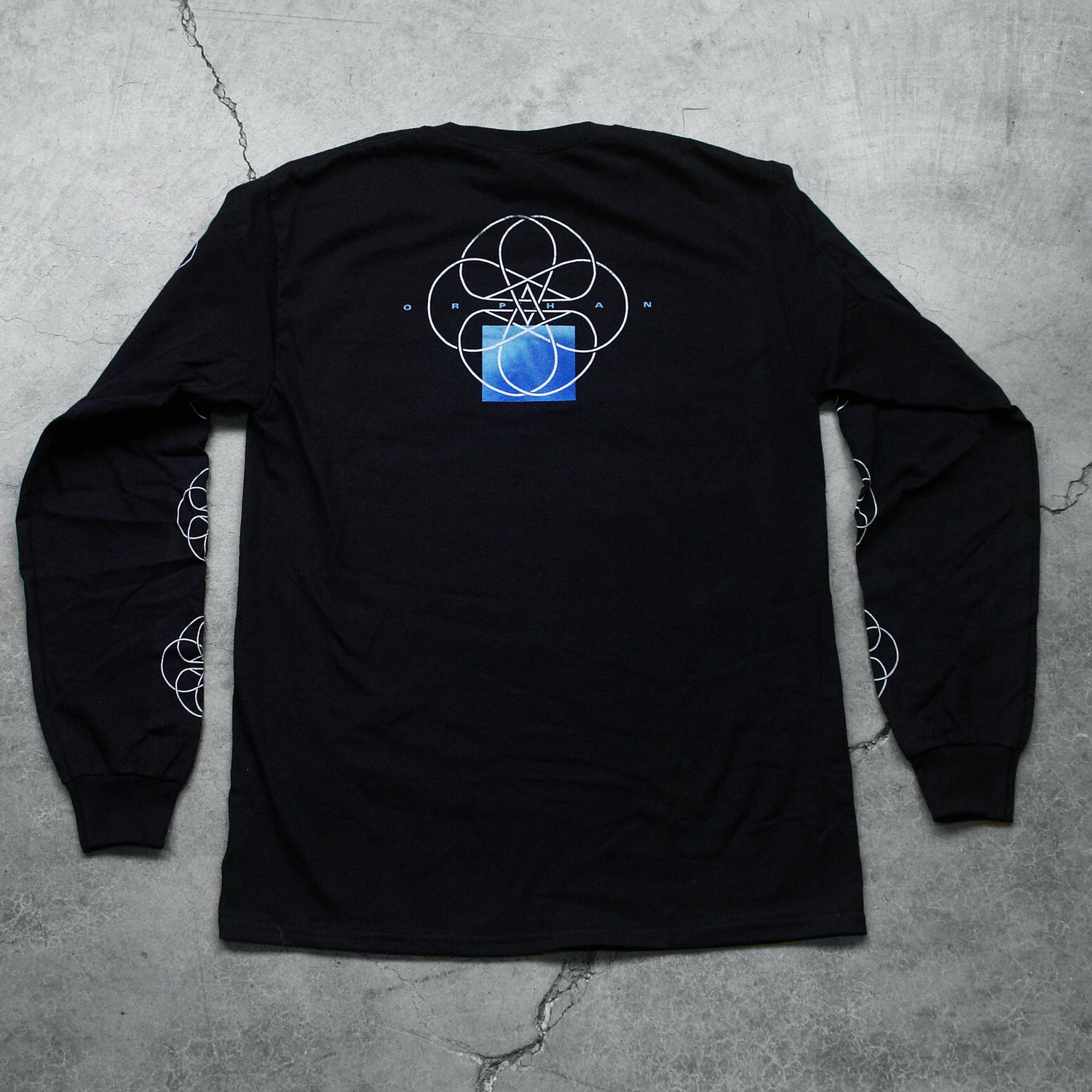  Image of the back of a black long sleeve against a grey concrete background. The sleeves feature a white circle abstract design with lines and two stars in the center making a double pentagram. The back center of the shirt near the shoulders features a white circle outline with abstract lines in the center, and two stars making a double pentagram. a blue square is underneath this. In small blue text reads 