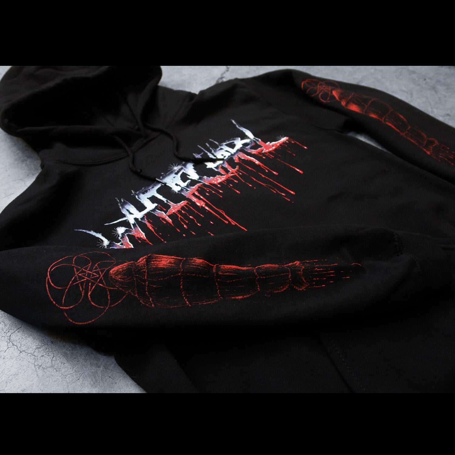 close up Image of the front of a black hoodie against a concrete grey background. Across the chest in a blue to white to red gradient color reads 